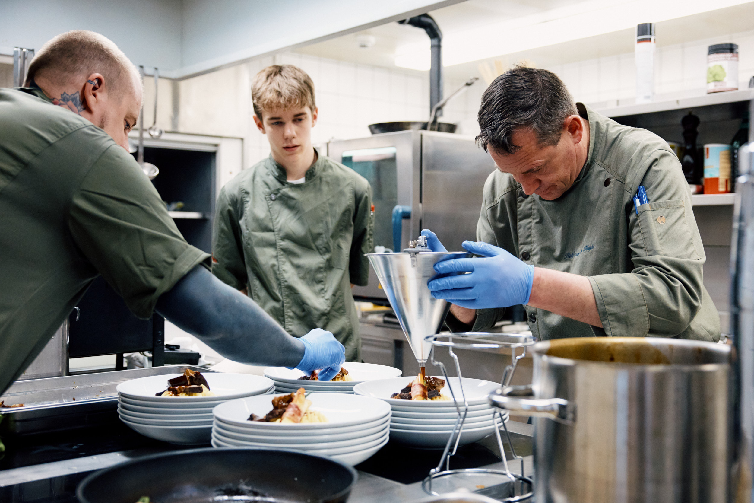 Arbeitssituation in der Küche des Hotels & Restaurants zum Schneggen: Betriebsleiter richtet einen Teller an, ein Lernender schaut zu, ein weiterer Mitarbeiter hilft beim Anrichten.